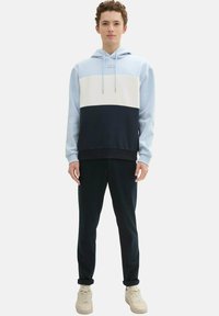 Jasnoniebieska, biała i granatowa bluza z kapturem w kolorowe bloki, związywana sznurkiem, zestawiona z ciemnymi spodniami i jasnymi trampkami. Miękka tkanina i luźny krój.