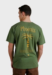 Zelené tričko s krátkým rukávem se žlutou grafikou palmy a textem na zadní straně, s volným střihem a měkkou texturou.