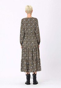 Robe noire à motifs floraux avec des manches longues, taille froncée et jupe à volants. Portée avec des bottines à lacets noires.