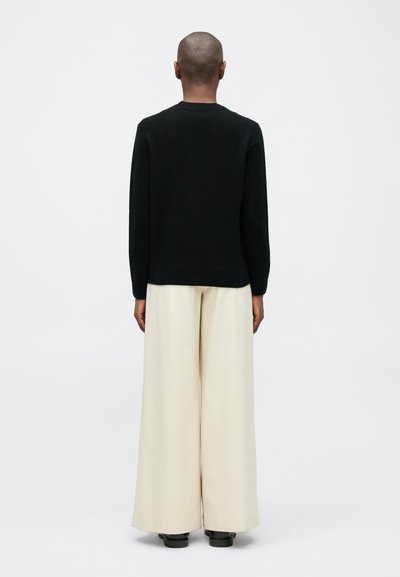 Suéter de punto negro de manga larga y cuello redondo, combinado con pantalones de pierna ancha color crema. El fondo es completamente blanco.