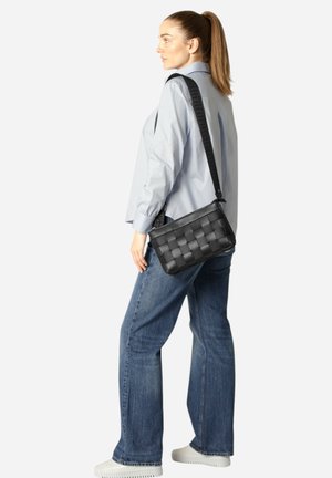 Bolso de mano de cuero trenzado negro con una larga correa para el hombro, forma rectangular, superficie texturizada y sutil detalle de costura.