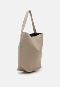 Béžová kožená taška přes rameno s texturovaným povrchem, měkkým tvarem a jedním ramenním popruhem. Uvnitř je černá podšívka.