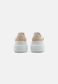Adidași albi cu accente din suede bej, o textură netedă și o talpă intermediară cu amortizare. Prezintă un spate rotund și un design clasic cu șireturi.