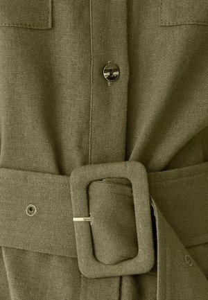 Tessuto verde oliva con finitura strutturata, caratterizzato da bottoni frontali, cintura in vita con fibbia rettangolare e una tasca sul petto singola.