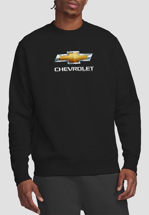 Schwarzer Sweatshirt mit einem großen, silbernen und goldenen Chevrolet-Logo, das auf der Brust zentriert ist. Ribbelbündchen und Saum. Weicher Stoff.