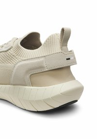 Baskets beige en tricot avec une semelle épaisse texturée, une languette en tissu et un maintien du talon en suède, vues de dos sur fond blanc.