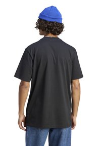 Czarny bawełniany t-shirt z krótkimi rękawami i luźnym fasonem, zestawiony z niebieską dzianą czapką typu beanie, widziany od tyłu.