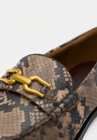 Mocassin en cuir à motif serpent marron et noir avec un accent métallique doré et un bout rond, présentant une texture lisse et des détails subtils.