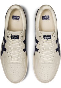 Cream leather sneakers with navy accents, featuring perforated toe box, lace-up closure, and branding on tongue. Classic athletic design.