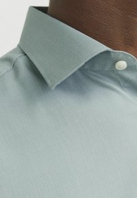 Lichtblauwe shirt met een gestructureerde stof, knoopkraag en een enkele witte knoopdetail aan de voorkant. Close-up van het kraaggebied.