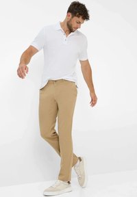 Witte poloshirt met korte mouwen, gecombineerd met kaki broek. Model draagt beige sneakers. Eenvoudig ontwerp, gladde textuur en neutrale kleuren.