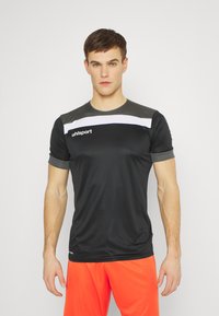 T-shirt de sport noir à manches courtes, avec des accents gris et une bande blanche sur la poitrine. Le tissu semble lisse et ajusté.