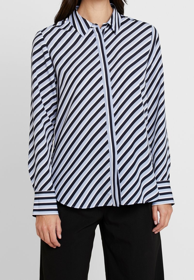 Chemise à manches longues boutonnée avec rayures bleu marine et bleu clair, dotée d'un col, d'une coupe structurée et de manches avec poignets. Texture de tissu doux.