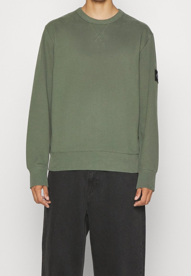 Groene crewneck sweatshirt met ribgebreide boorden en zoom, voorzien van een patchlogo op de linkermouw, gemaakt van zacht materiaal, met een casual pasvorm.