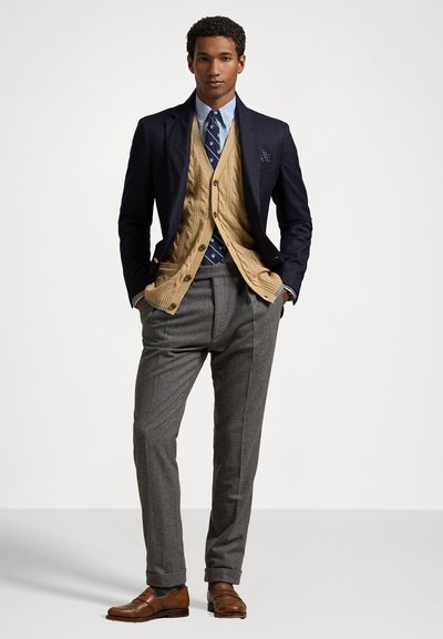 Jūras spēku tumši zils bleiseris virs adītas smilškrāsas vestes, gaiši zila krekla, rakstainā kaklasaites, pelēku biksēm un brūnām mokasīnām. Vienkārša kabatas lakatiņa detaļa.