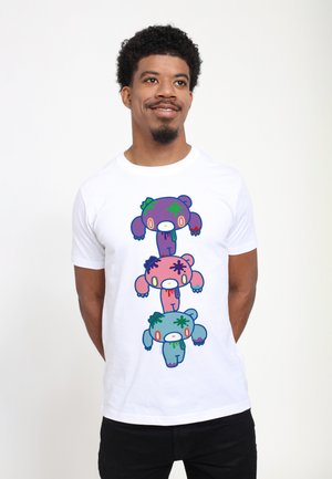 Homme aux cheveux courts et bouclés portant un t-shirt blanc avec une pile verticale de trois ours dessin animé colorés avec des éclaboussures de peinture.