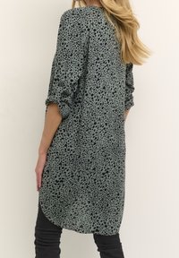 Camisa larga de estampado de leopardo verde, hecha de tejido ligero, con dobladillo redondeado y mangas enrolladas.