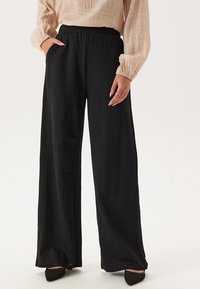 Zwarte wijde broek van een gestructureerde stof, met een hoge elastische tailleband en zijzakken, gecombineerd met een lichte, gestructureerde blouse.