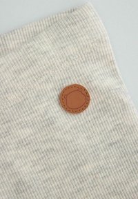 Bawełniany sweter o ribbowanej fakturze w jasnym beżu, z brązową okrągłą naszywką ze skóry, przyszytą z boku.