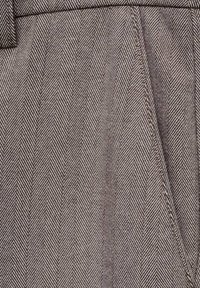 Tissu en chevron brun avec un tissage texturé, présentant des lignes diagonales et des variations subtiles de teinte pour créer de la profondeur. Gros plan sur les détails du matériau.