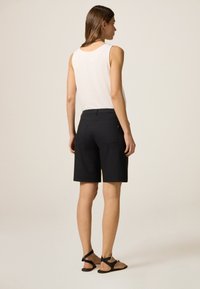 Shorts noirs à coupe ajustée, avec une texture lisse, deux poches arrière et une taille mi-haute, associés à un haut sans manches blanc.