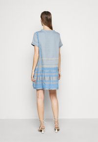 Modrá šaty s krátkým rukávem s texturovaným vzorem, vrstevnatou sukňovou designem a volným střihem, doplněné béžovými sandály na podpatku.