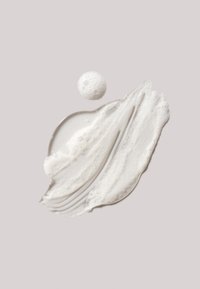 Producto blanco y cremoso con una textura suave y brillante y burbujas, aplicado en una forma curva sobre un fondo gris suave.