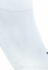 Calcetín deportivo blanco hecho de tejido transpirable, con un fino canalé y una textura suave. Incluye un detalle del logo negro en el costado.