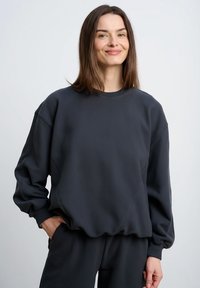 Ciemnoszara bluza z okrągłym dekoltem i ściągaczami na r�ękawach. Charakteryzuje się luźnym krojem i subtelnymi ukośnymi szwami. Miękka w dotyku.