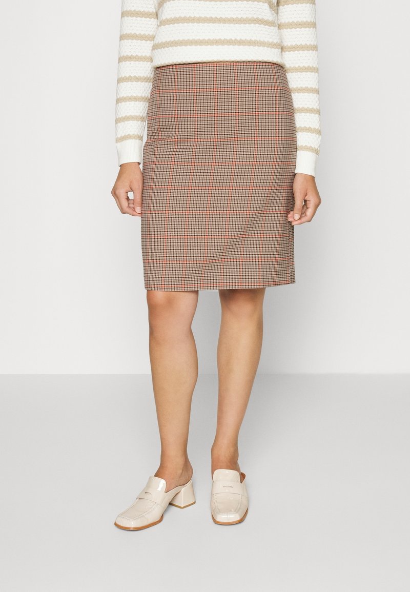 Falda lápiz a cuadros en marrón con acentos rojos, hecha de tela tejida. Diseño entallado de longitud media con una textura suave. Combinada con mules claros.