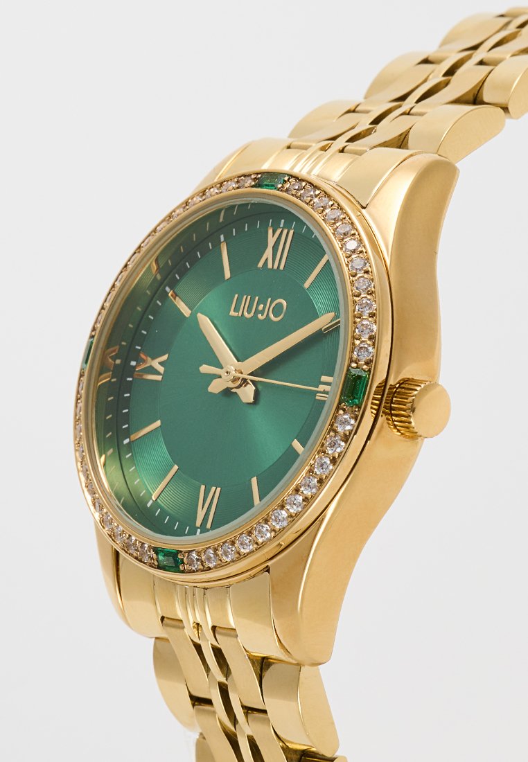 Montre dorée avec cadran vert, chiffres romains et accents ressemblant à des diamants autour de la lunette. Équipée d'un bracelet en acier inoxydable avec maillons polis.