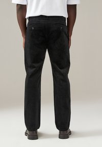 Pantaloni in corduroy neri con taglio dritto, sottili righe verticali e due tasche posteriori con chiusura a bottone.