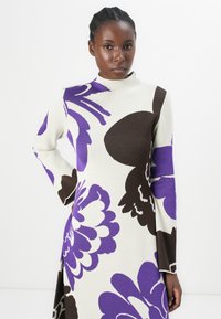 Knit dress featuring bold purple and brown floral patterns on a cream background. High neck, long sleeves, and fitted design.