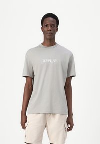 Camiseta de algodón gris con cuello redondo y mangas cortas, que presenta una impresión blanca de "REPLAY SINCE 1981" en el frente.