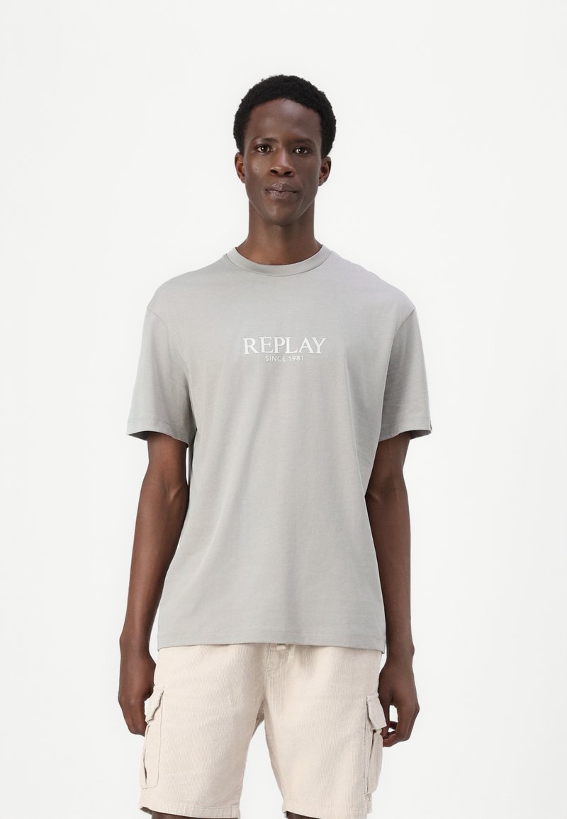Camiseta de algodón gris con cuello redondo y mangas cortas, que presenta una impresión blanca de "REPLAY SINCE 1981" en el frente.