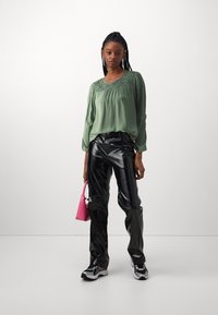 Grønn bluse med blonder, svarte blanke bukser og rosa håndveske. Sneakers med svart og hvit aksenter fullfører antrekket.