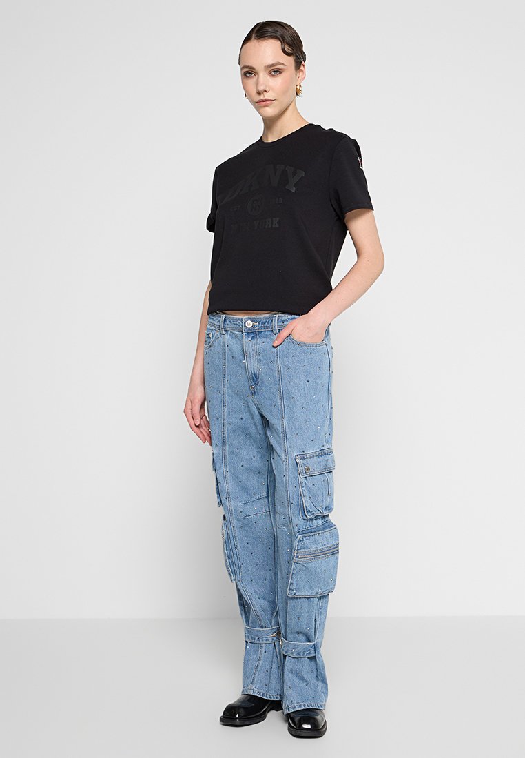 Schwarzes T-Shirt mit Rundhalsausschnitt und bedrucktem Logo, kombiniert mit hellblauen Denim-Cargohosen mit mehreren Taschen und einer lockeren Passform.