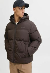 Bruine puffy jack met een capuchon, met gequiltte secties en een rits aan de voorkant. Logo op de linkerkant van de borst, zijzakken en elastische manchetten.
