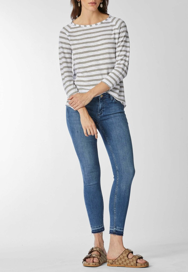 Striped gray and white long-sleeve top paired with fitted blue jeans and brown patterned sandals. Simple design, relaxed fit, and casual style.