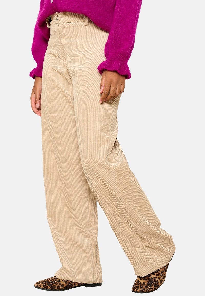 Beige Corduroy-Hosen mit weitem Bein sind mit vertikalen Rippungen, hoher Taille und einem entspannten Schnitt versehen. Kombiniert mit einem knallpinkem Pullover und Schuhen im Leopardenmuster.