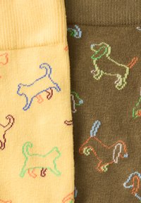 Κίτρινες και καφέ κάλτσες με παιχνιδιάρικες κεντητές σχεδιάσεις σκύλου ντάτσχουντ σε διάφορα χρώματα. Η κίτρινη κάλτσα έχει πολύχρωμες σχέσεις, ενώ η καφέ κάλτσα έχει πιο σκούρο, υφασμάτινο φόντο.