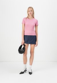 Haut à manches courtes côtelé rose associé à une mini-jupe en denim foncé, des escarpins noirs à bout pointu, des chaussettes blanches et un sac à main noir.