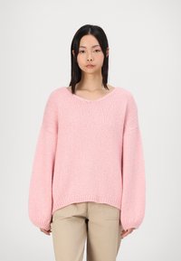 Maglione rosa lavorato a maglia con una vestibilità ampia, maniche larghe e scollatura a V. Tessuto morbido con orlo a coste e un delicato motivo a punto.