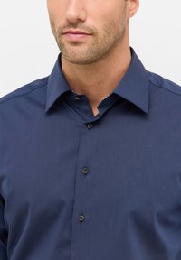 Camicia blu navy con bottoni, colletto strutturato, texture liscia e interno a contrasto con motivo. Dotata di bottoni marroni.