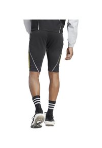 Zwarte sportshorts met gele accenten, met een aansluitend ontwerp, elastische tailleband en reflecterende stiksels. Draagt met zwart-witte gestreepte sokken.