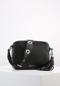 Borsa a tracolla in pelle nera con finitura testurizzata, hardware in tonalità argento, tracolla regolabile e dettaglio con nappina. Presenta il logo del marchio sul fronte.