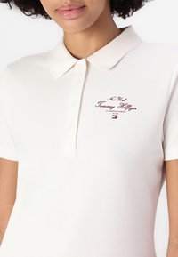 Polo marškiniai švelnaus bežinio medvilnės, su klasikinėmis apykaklėmis, trimis sagomis ir bordo siuvinėjimu, kuriame išsiuvinėtas "Tommy Hilfiger" logotipas.