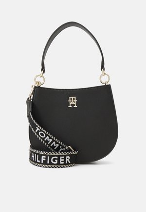 Sort læder skuldertaske med et gyldent "TH" logo og en aftagelig sort og hvid "Tommy Hilfiger" stofrem.