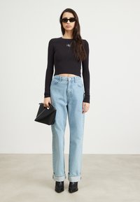 Sort ribbet crop top med logo, lyseblå højtaljede jeans, sorte spidse ankelstøvler og en lille sort håndtaske.