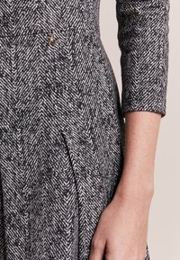 Tissu de robe à motif chevron noir et blanc avec une silhouette structurée, doté d'un accent décoratif doré près de la taille.